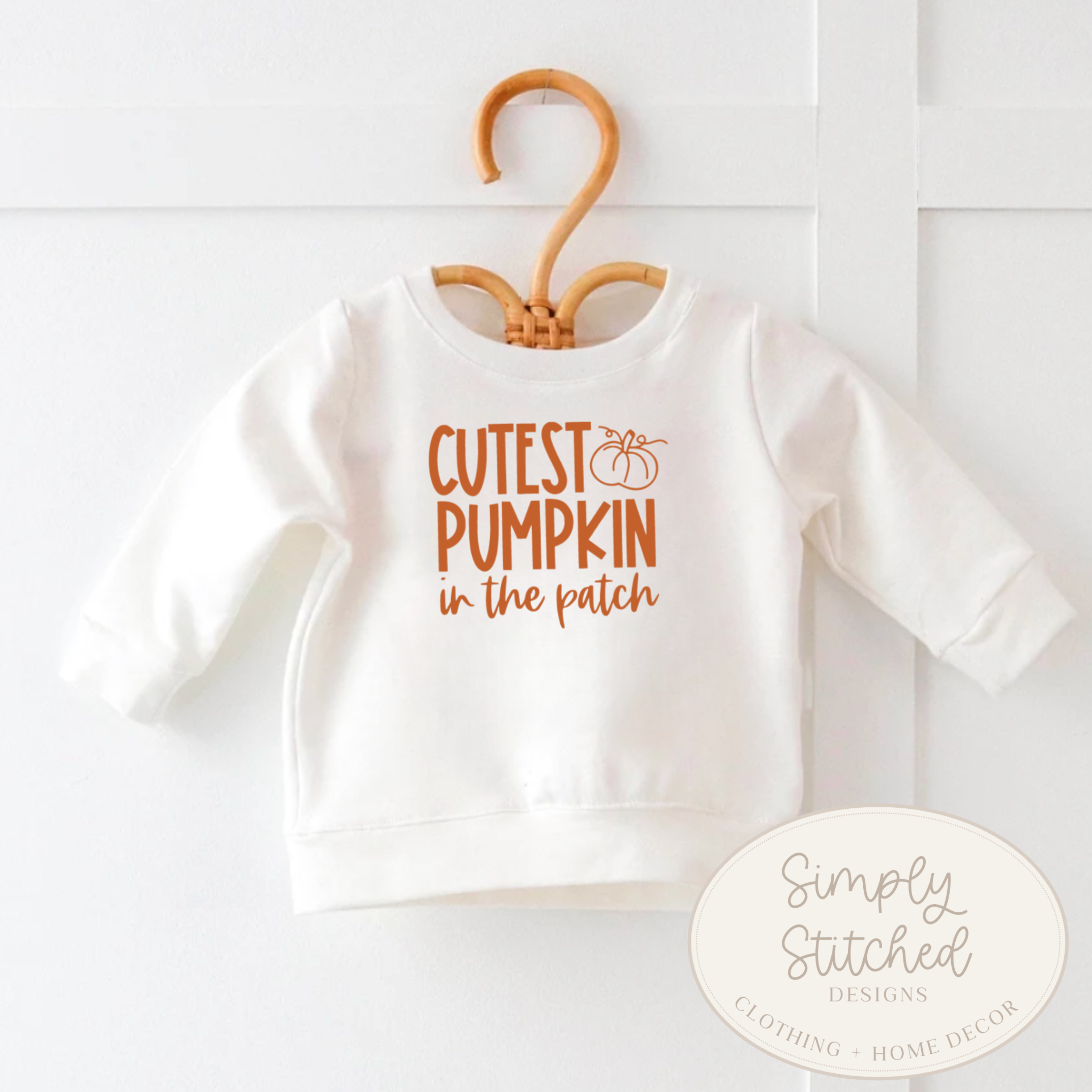 White baby sweater with 'Cutest Pumpkin in the Patch' text on a hanger, brand 'Simply Stitched' visible.