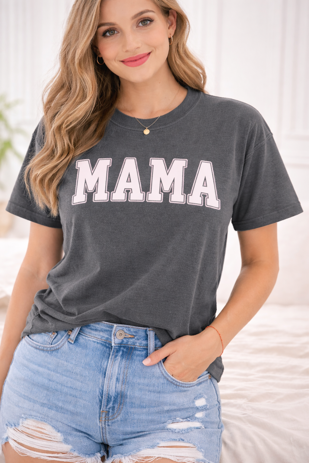 Woman wearing a gray t-shirt with 'MAMA' text and ripped jeans indoors.